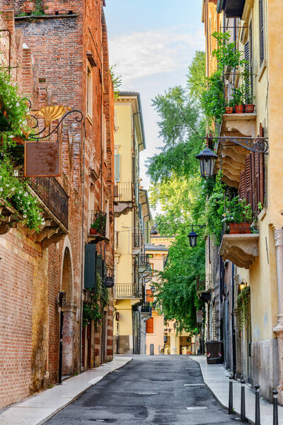 View of narrow street at historic centre of Verona, Italy. Facades of houses in morning sun. Verona is a popular tourist destination of Europe.