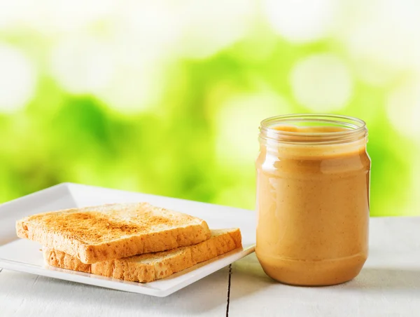 Tarro de mantequilla de maní y tostadas sobre fondo natural —  Fotos de Stock