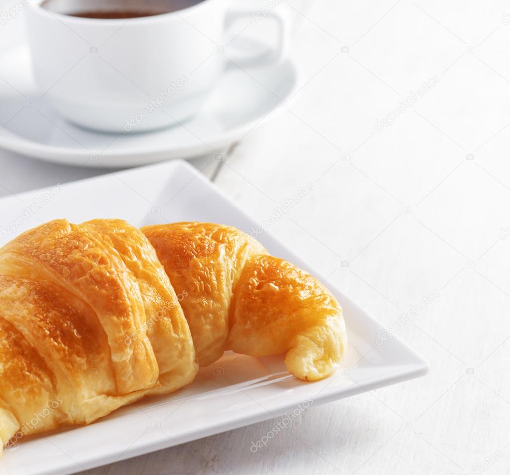Cup of coffee and croissant on white wooden table