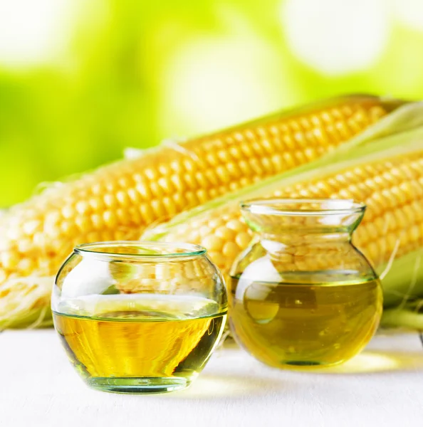 Кукурузное масло и кукурузные початки на садовом столе — стоковое фото