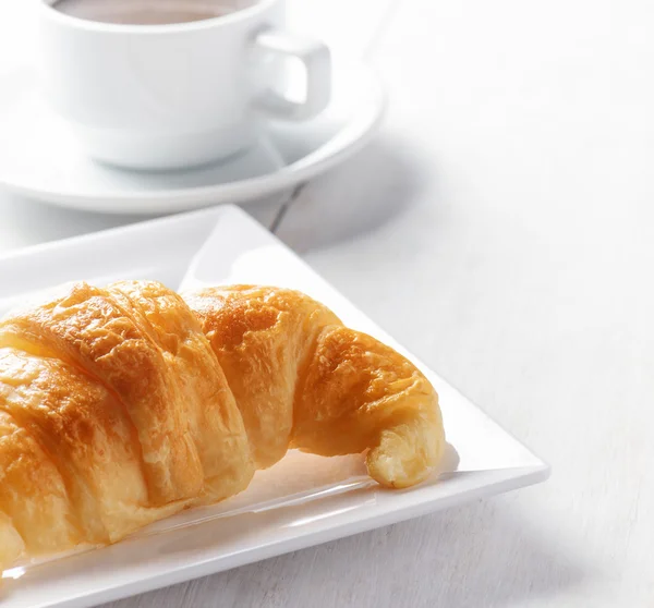 Šálek kávy a croissantu na bílý dřevěný stůl — Stock fotografie