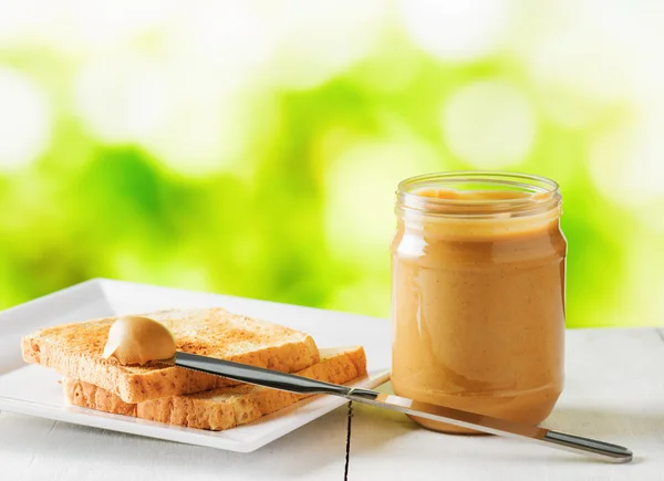 Jar of peanut butter and toasts on nature background — Stock Photo, Image