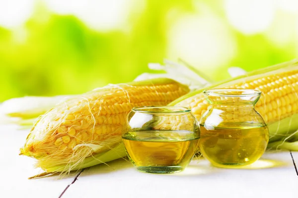 Кукурузное масло и кукурузные початки на садовом столе — стоковое фото