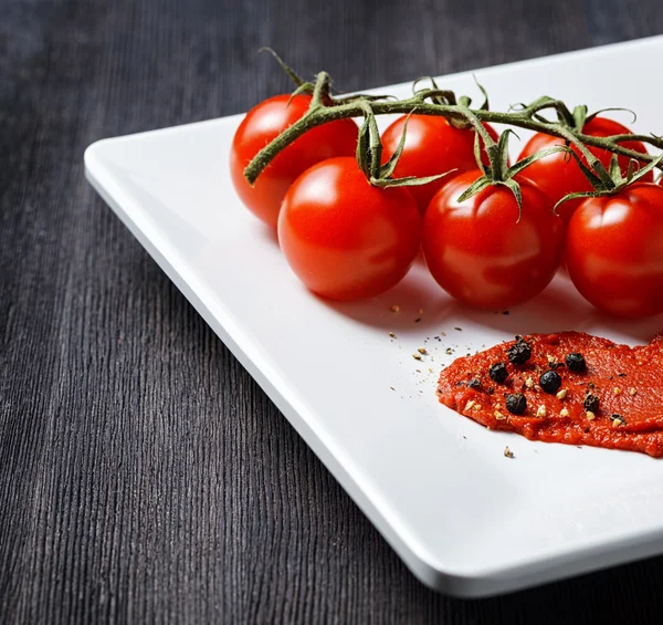 Tomates maduros y pasta de tomate en un plato blanco sobre una mesa de madera — Foto de Stock