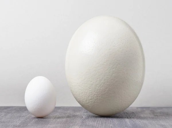 Страусиное яйцо и куриное яйцо на черном столе — стоковое фото
