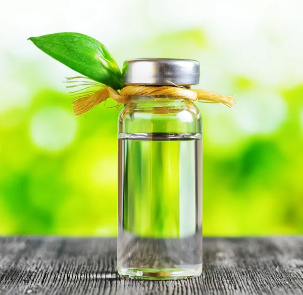 Vial of liquid on a black wooden table and on nature background — Stock Photo, Image