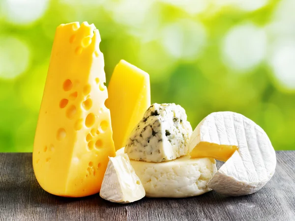 Different types of cheese on a black wooden table and on nature — Stock Photo, Image