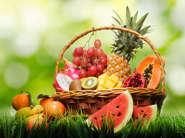 Basket of fresh tropical fruits on green grass and on nature bac