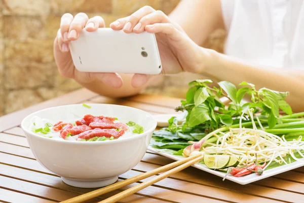 Jovem mulher tirando uma foto do Pho Bo no smartphone no Vietnã — Fotografia de Stock