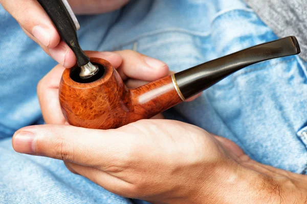 Man holding smoking pipe in hand and tamping down tobacco — Stockfoto