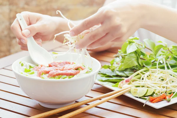 Young woman sprinkles sprouts to the Pho Bo in cafe, Vietnam — Stock Photo, Image