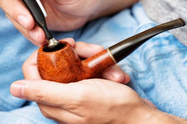 Young man holding smoking pipe in hand and tamping down tobacco