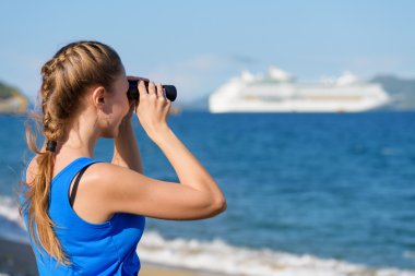 Young female tourist looking through binoculars at cruise liner