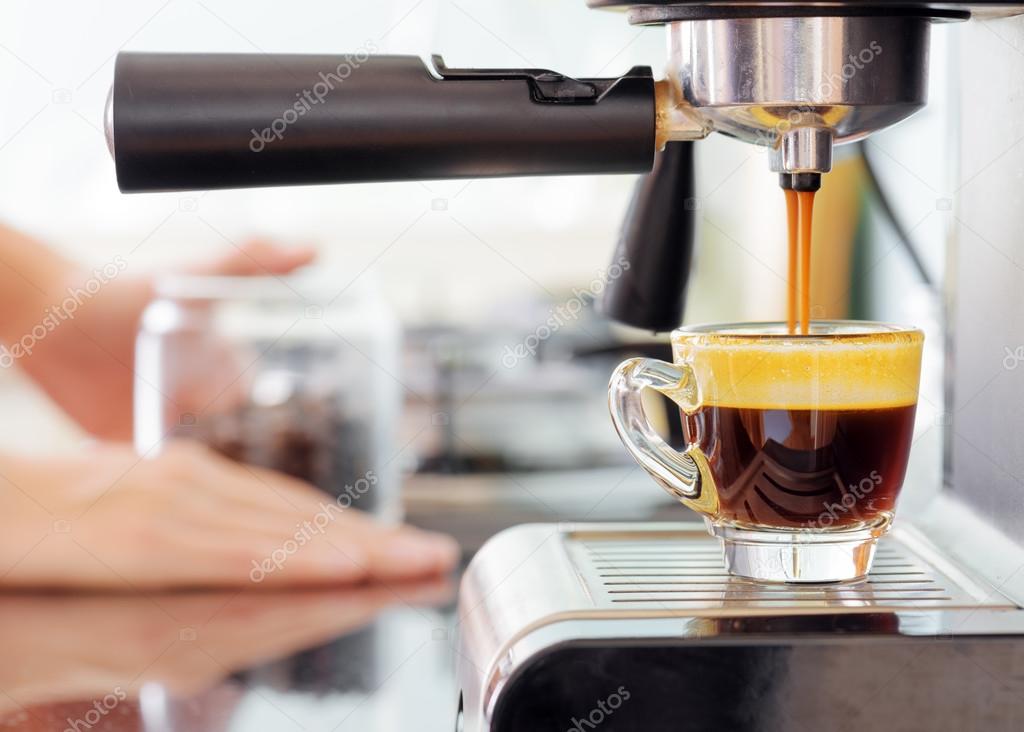 Espresso coffee machine in kitchen. Hot coffee pouring into cup