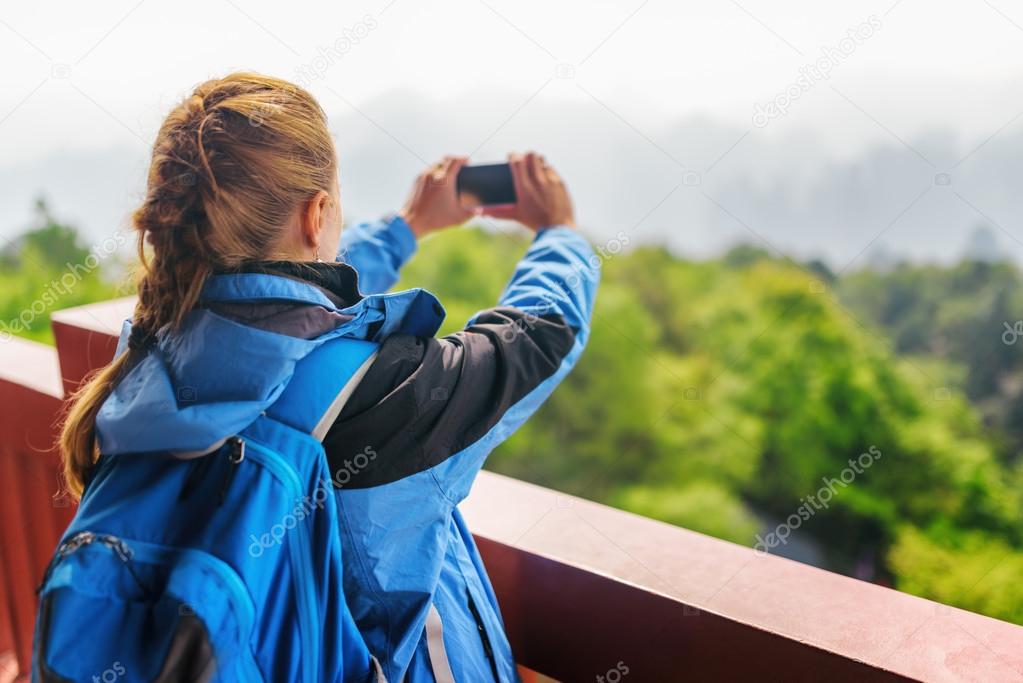 Young female tourist with smartphone taking photo of mountains