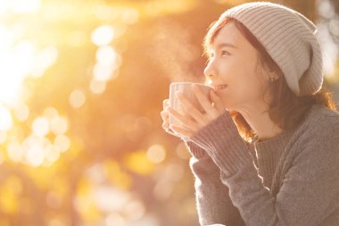 Mutlu kadın sonbahar parkında kahve içiyor.
