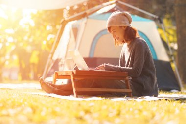 Genç kız kamp çadırında dizüstü bilgisayar kullanıyor, sonbahar ormanlarında yürüyüş yapıyor.