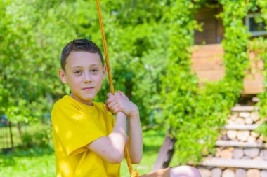 Sarı tişört lastik salıncak üzerinde oynama çocukta gülümseyerek