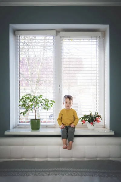 Pequeño chico solitario sentado en el alféizar de la ventana — Foto de Stock