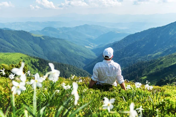 A tourist in white clothes sits in a mountain meadow — Stock Photo, Image