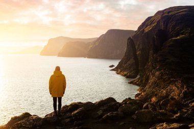 Sarı ceketli turist Sorvagsvatn Gölü yakınlarındaki kayalıklara bakıyor.