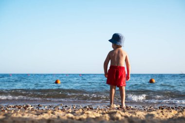 Yaz plajında kırmızı şortlu bir çocuk.
