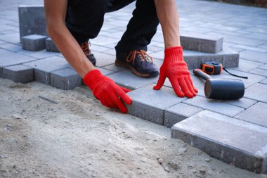 Sarı eldivenli usta kaldırım taşları serer.