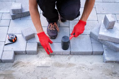 Sarı eldivenli usta kaldırım taşları serer.