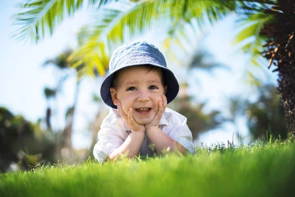 Счастливый маленький мальчик лежит на зеленой траве под пальмами — стоковое фото