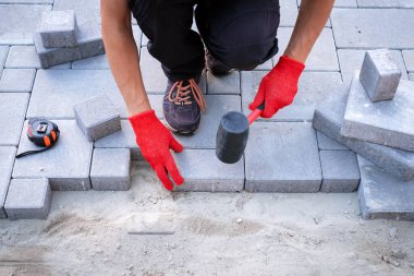 Sarı eldivenli usta kaldırım taşları serer.