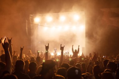 Parlak sahne ışıkları önünde konser kalabalığının siluetleri