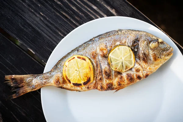 Pescado dorada a la parrilla con trozos de limón en plato blanco —  Fotos de Stock