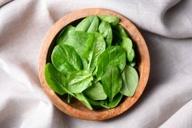 Düz yeşil ıspanak bej keten kumaşın üzerinde ahşap kasede dizilmiş. Doğal mutfak dekorasyonu, sürdürülebilir yaşam tarzı ve taze üretim konsepti