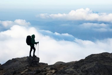 Sırt çantalı bir turist bulutların ve dağların arkasında duruyor. Seyahat ve macera konsepti