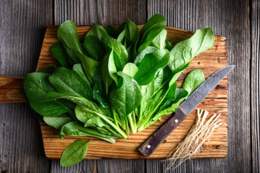 Kırsal ahşap tahtadaki taze ıspanak yapraklarının yanında bıçak ve kökleri var. Taze ürün, mutfak hazırlığı ve sürdürülebilir yaşam tarzı kavramı