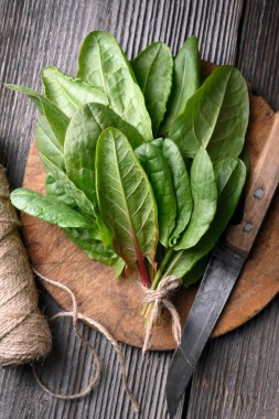 Mutfak bıçağı ve doğal iplikle dairesel kesim tahtasının üzerinde yeşil kuş yaprağı, yukarıdan görüş. Düzleştirme, organik sebzeler, yemek hazırlama konsepti.