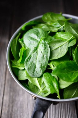 Eskimiş ahşap masanın üzerinde koyu arkaplana karşı kırsal metal kevgire batırılmış taze ıspanak yaprakları. Organik sebzeler, sağlıklı beslenme ve doğal gıda tasarımı.