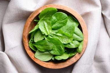 Yumuşak keten kumaşın üzerine yerleştirilmiş ahşap kasedeki organik ıspanak yapraklarının üst görüntüsü. Bitki temelli diyet, doğal malzemeler ve gıda fotoğrafçılığı konsepti