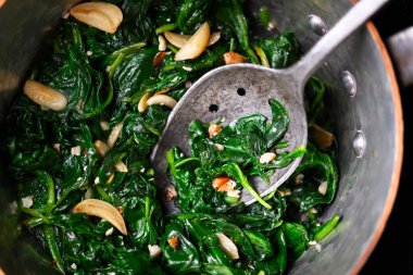 Sarımsak ve fındık parçalarıyla birlikte kaliteli bakır tencerede servis edilen sıcak sotelenmiş ıspanak. Çiftlikten sofra mutfağına, doğal malzemeler ve gıda tasarım konsepti.