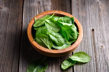 Parlak yapraklı ıspanak ahşap sehpanın üzerinde ahşap kasede dizilmiş, yakın plan. Taze sebzeler, sürdürülebilir yaşam tarzı ve sağlıklı beslenme konsepti.