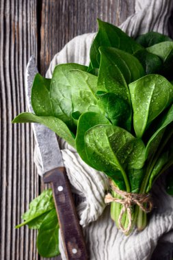 Mutfak havlusuna ip bağlanmış taze ıspanak demetinin ahşap masa üzerindeki üst görüntüsü. Çiftlik hasadı, kırsal gıda tasarımı ve sürdürülebilir aşçılık konsepti