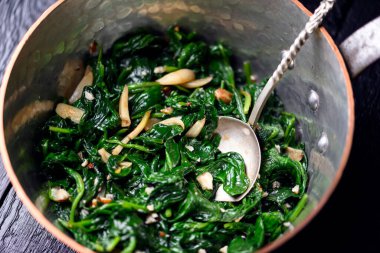 Bakır tencereli ıspanak sotesi ve ahşap kaplamalı kaşık. Sanatsal mutfak eşyaları, taze tarifler ve sağlıklı yaşam tarzı konsepti.