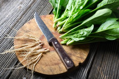 Yuvarlak ahşap kesme tahtasındaki taze ıspanak yaprakları yanında da bıçak ve kökleri var. Taze ürün, mutfak hazırlığı ve sürdürülebilir yaşam tarzı kavramı