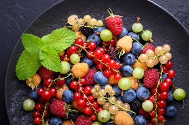Seramik tabakta çeşitli orman meyvelerinin genel bileşimi. Kırmızı ve beyaz frenk üzümü, yabanmersini, ahududu, bektaşi üzümü, taze organik hasat