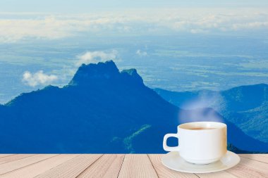 Sabahları dağ manzaralı ahşap bir masada bir fincan kahve.