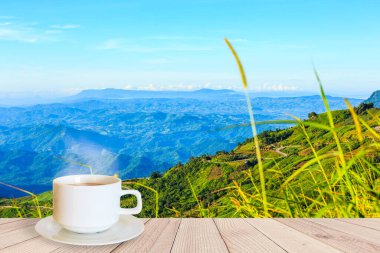 Sabahları dağ manzaralı ahşap bir masada bir fincan kahve.
