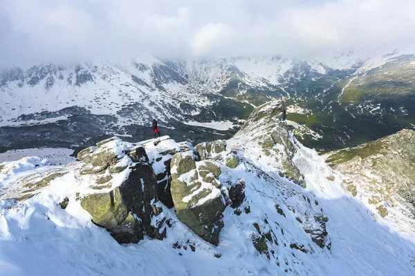 Landscape on the cold winter morning. Happy tourist in sport clothes is standing at the edge of the precipice. High mountains with snow white peaks. Snowy background. Nature scenery. Location place the Carpathian, Ukraine, Europe.