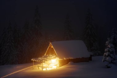 Kış gecesi. Işıklı ev. Geniş yol karlı eski ahşap kulübeye gidiyor. Yüksek dağların ve ormanların manzarası. Karla kaplı çimenler. Konum: Carpathian, Ukrayna, Avrupa.