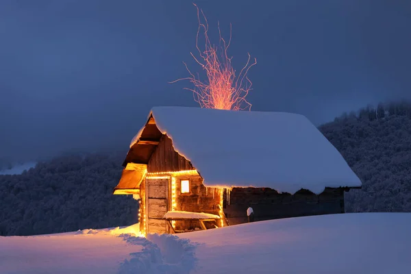 Winter landscape. Mystical night. Old wooden hut on the lawn covered with snow. The lamps light up the house at the evening time. Mountains and forests. Wallpaper background.