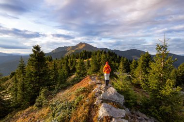Güzel bulutlu gökyüzü manzarası. Sonbahar sabahı dağları. Başarılı sporcu kız, çimlerin üzerinde turuncu ceketle duruyor. Duvar kağıdı arka planı. Carpathian, Ukrayna, Avrupa 'yı rahatlatacak bir yer..